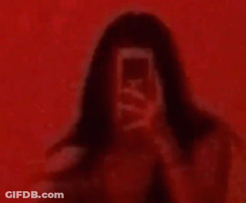 A Woman Is Taking A Picture Of Herself In Front Of A Red Wall . GIF