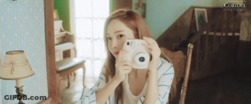 A Woman Is Taking A Picture Of Herself With A White Camera . GIF