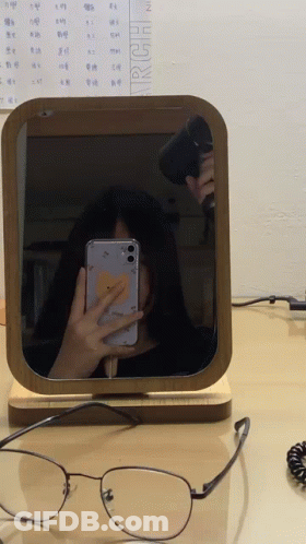 A Woman Is Taking A Selfie In Front Of A Mirror With A Calendar Behind Her That Says March GIF