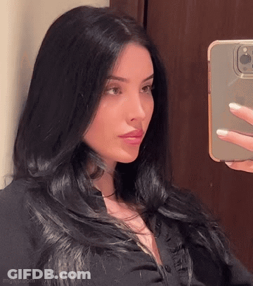 A Woman Is Taking A Selfie In Front Of A Mirror With Her Cell Phone . GIF