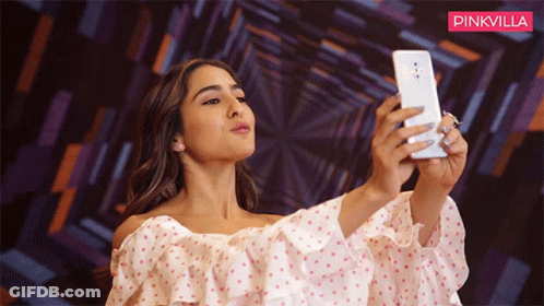 A Woman Is Taking A Selfie In Front Of A Pinkvilla Banner GIF