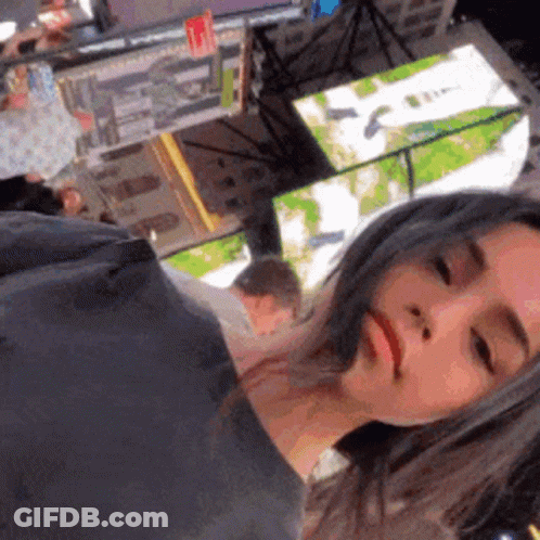 A Woman Is Taking A Selfie With Her Eyes Closed In Front Of A Large Screen . GIF