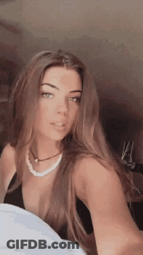 A Woman Is Taking A Selfie With Her Phone While Wearing A Black Top And A Pearl Necklace . GIF