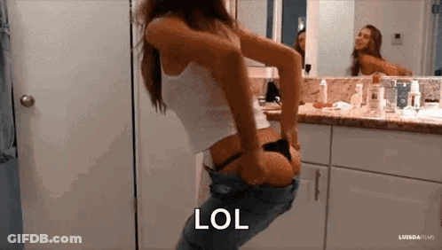 A Woman Is Taking Off Her Pants In Front Of A Mirror . GIF