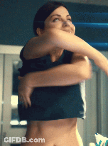 A Woman Is Taking Off Her Shirt And Looking At The Camera GIF