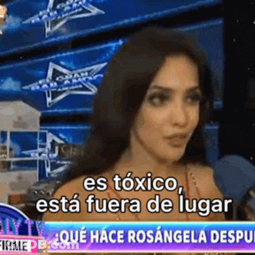 A Woman Is Talking Into A Microphone In Front Of A Sign That Says " Es Toxico " GIF