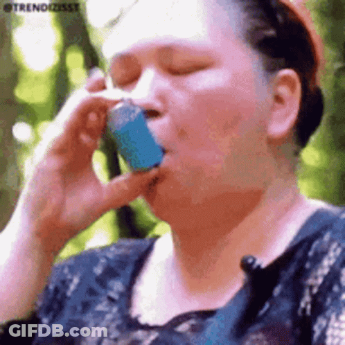 A Woman Is Talking On A Cell Phone While Holding A Blue Asthma Inhaler In Her Mouth . GIF