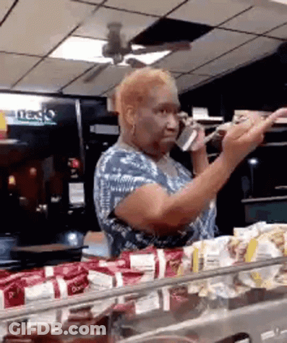 A Woman Is Talking On A Cell Phone While Standing In Front Of A Counter . GIF