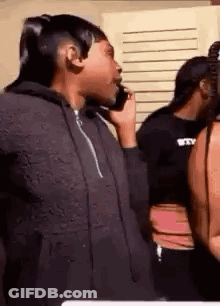 A Woman Is Talking On A Cell Phone While Standing Next To Another Woman . GIF