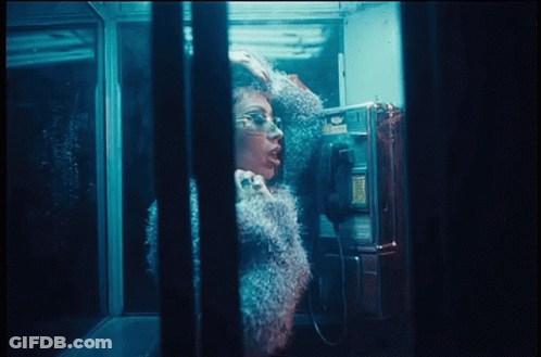 A Woman Is Talking On A Pay Phone In A Booth GIF