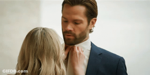 A Woman Is Touching A Man 'S Tie While He Is Wearing A Suit And Tie . GIF