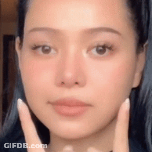 A Woman Is Touching Her Face With Her Hands . GIF