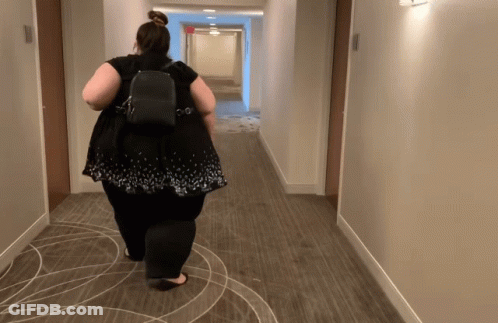 A Woman Is Walking Down A Hallway With A Backpack GIF