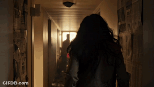 A Woman Is Walking Down A Hallway With Newspapers Hanging On The Walls GIF