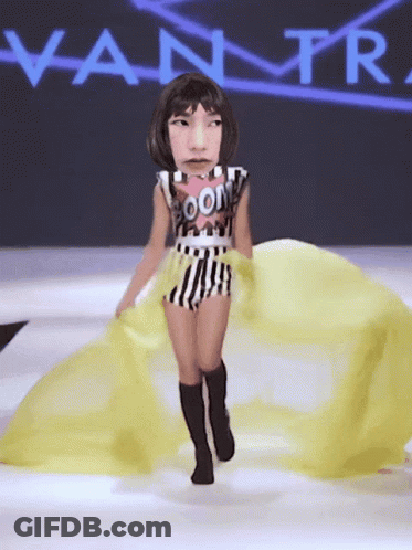 A Woman Is Walking Down A Runway With A Vanity Fair Logo Behind Her GIF