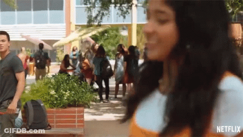 A Woman Is Walking Down A Sidewalk In Front Of A Crowd Of People And A Netflix Logo . GIF