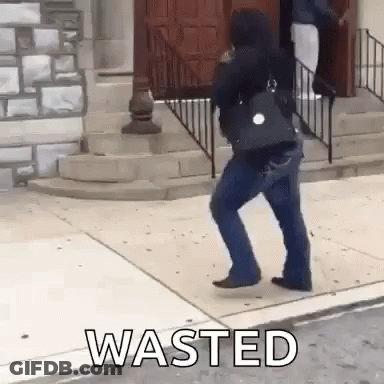 A Woman Is Walking Down A Sidewalk Next To A Building With The Word Wasted On The Sidewalk . GIF