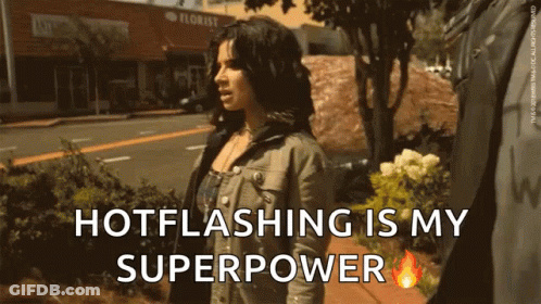 A Woman Is Walking Down A Sidewalk With The Words Hotflashing Is My Superpower GIF