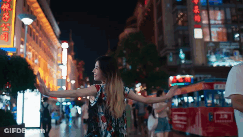 A Woman Is Walking Down A Street At Night With A Sign That Says ' Chinese ' On It GIF