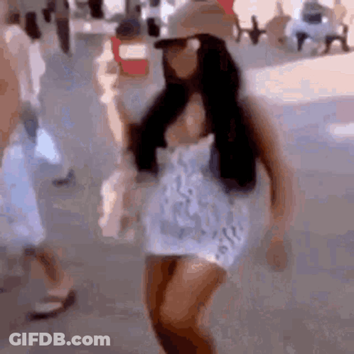 A Woman Is Walking Down A Street Wearing A Hat And Sunglasses . GIF