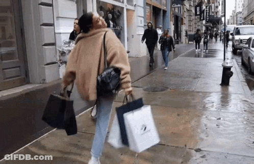 A Woman Is Walking Down The Street Carrying Shopping Bags GIF