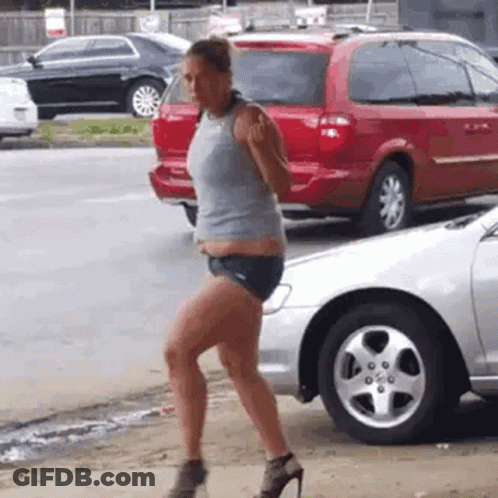 A Woman Is Walking Down The Street Next To A Silver Car . GIF