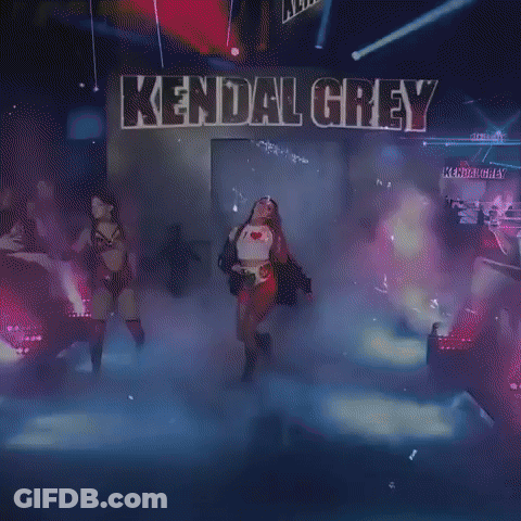 A Woman Is Walking On A Stage In Front Of A Sign That Says Kendall Grey . GIF