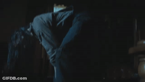 A Woman Is Walking Through A Dark Room With A Window Behind Her GIF