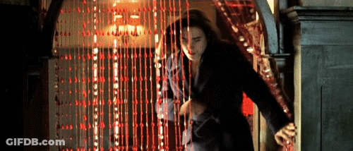 A Woman Is Walking Through A Doorway With A Red Curtain Behind Her . GIF
