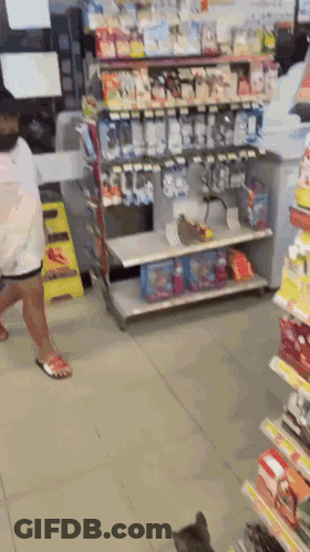 A Woman Is Walking Through A Store Aisle With A Cat GIF