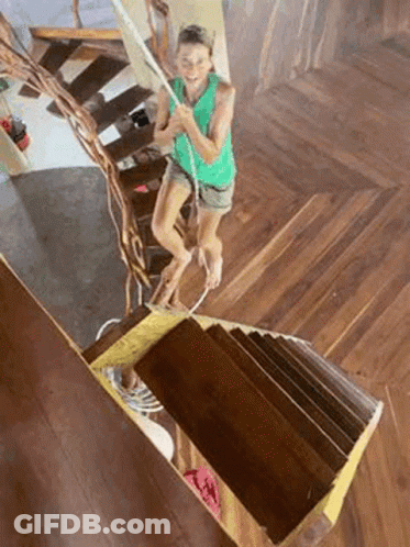 A Woman Is Walking Up A Set Of Wooden Stairs . GIF