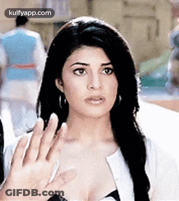 A Woman Is Waving Her Hand In The Air While Standing In Front Of A Crowd . GIF