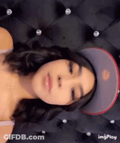 A Woman Is Wearing A Baseball Cap And Laying On A Bed . GIF