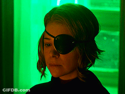 A Woman Is Wearing A Black Eye Patch In Front Of A Green Light . GIF