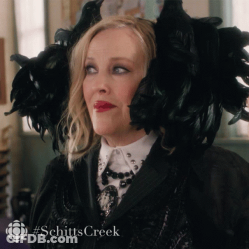 A Woman Is Wearing A Black Feathered Hat With The Hashtag Schitts Creek On The Bottom GIF