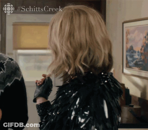 A Woman Is Wearing A Black Jacket And Gloves With #Schitts Creek On The Bottom GIF