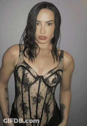 A Woman Is Wearing A Black Lace Bodysuit With A Plunging Neckline GIF
