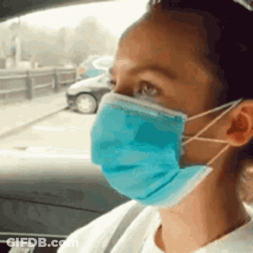 A Woman Is Wearing A Blue Face Mask While Sitting In A Car . GIF
