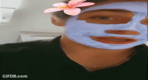 A Woman Is Wearing A Blue Mask On Her Face With A Pink Flower In Her Hair . GIF