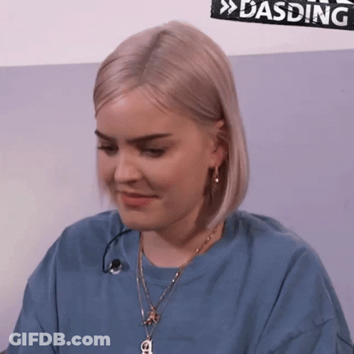 A Woman Is Wearing A Blue Shirt And A Necklace With A Letter A On It GIF