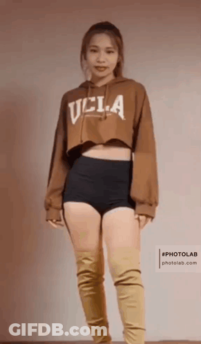 A Woman Is Wearing A Brown Ucla Hoodie And Black Shorts GIF
