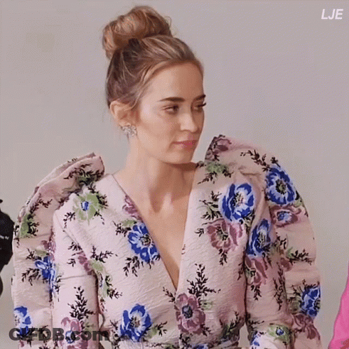A Woman Is Wearing A Floral Dress With Puffed Sleeves And A Bun In Her Hair GIF