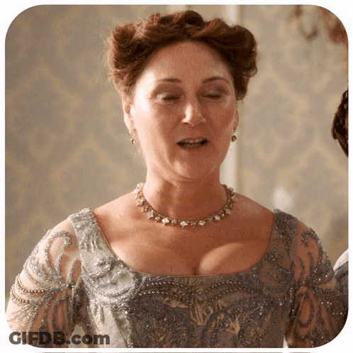 A Woman Is Wearing A Necklace And Earrings And A Gray Dress GIF