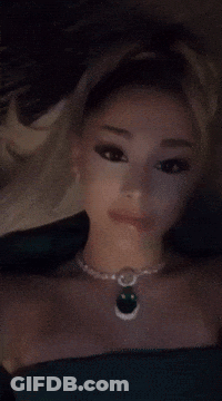 A Woman Is Wearing A Necklace With A Green Pendant GIF