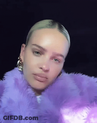 A Woman Is Wearing A Purple Fur Coat And Earrings . GIF