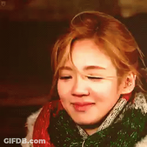 A Woman Is Wearing A Scarf Around Her Neck And Smiling . GIF