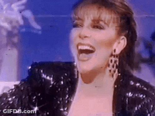 A Woman Is Wearing A Sequined Jacket And Earrings And Laughing . GIF