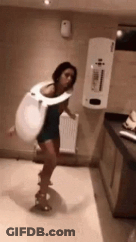 A Woman Is Wearing A Toilet Seat Costume And Dancing In A Bathroom . GIF