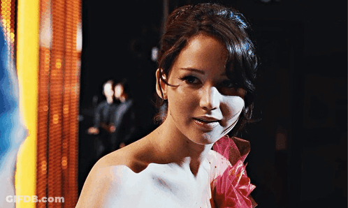 A Woman Is Wearing A White Dress With A Pink Flower On The Shoulder GIF