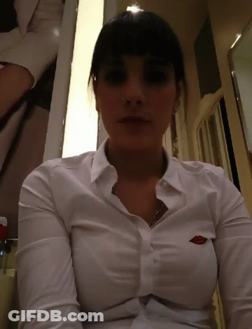 A Woman Is Wearing A White Shirt With A Logo On The Breast GIF